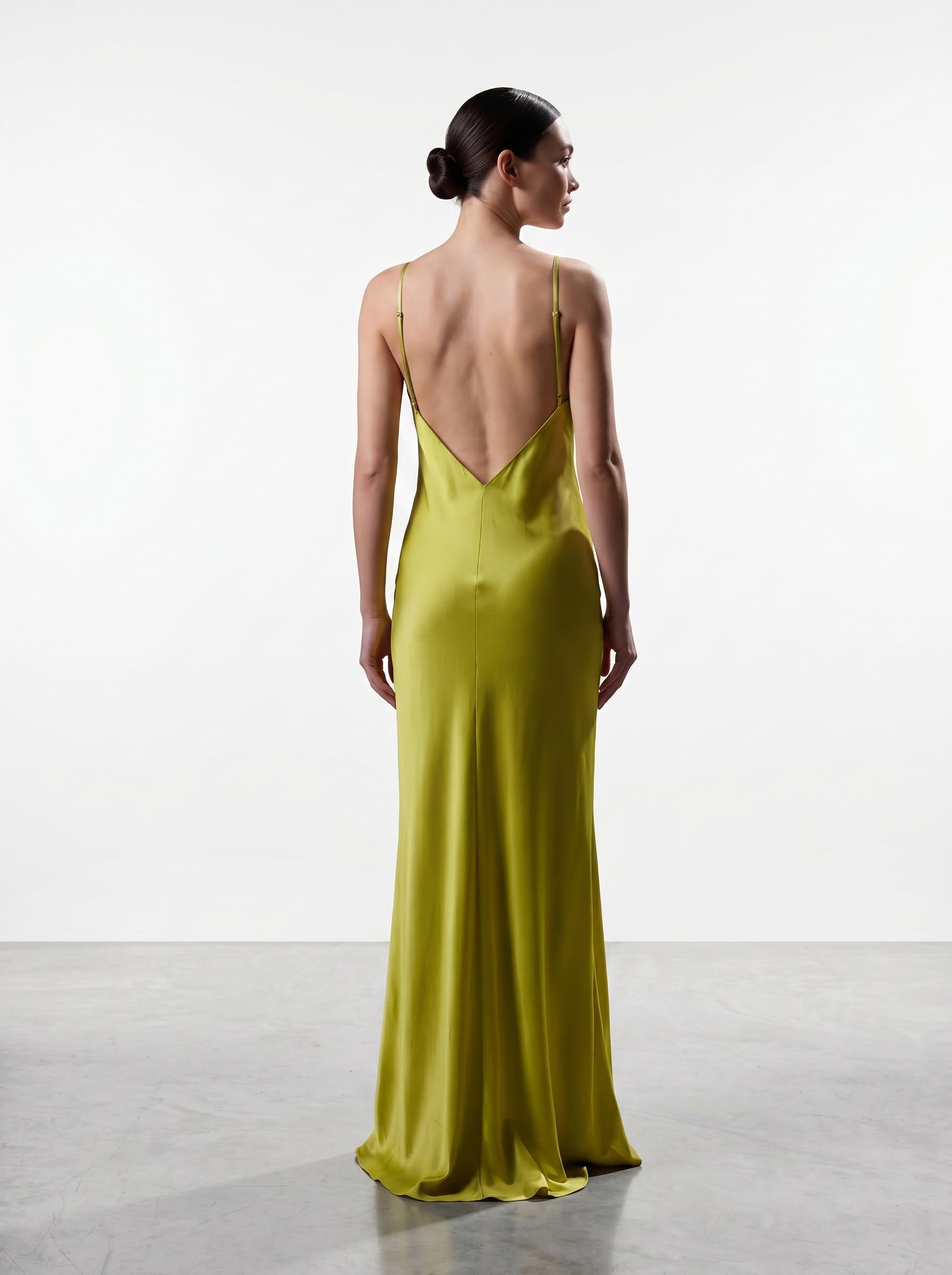 Woman wearing a long, light green dress with a backless design on a white background