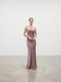 Woman in a pink satin gown standing in a spotlight against a plain background